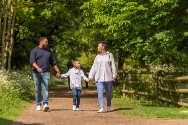 A couple and their child hold hands on a woodland walk.