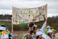 Children hold up a flag with trees on at Arbor Day celebrations.