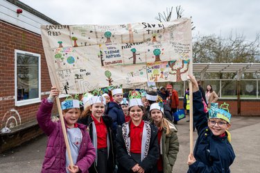 Children hold up a flag with trees on at Arbor Day celebrations.