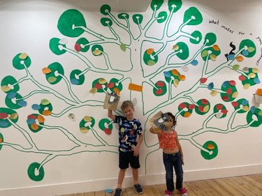 Two children stand in front of an interactive mural that reads "What makes a great childhood?"