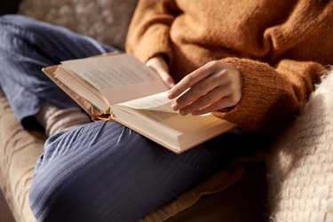 A closeup of a person reading a book balanced on their lap.