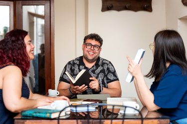 Friends reading and talking about books at a cafe table.